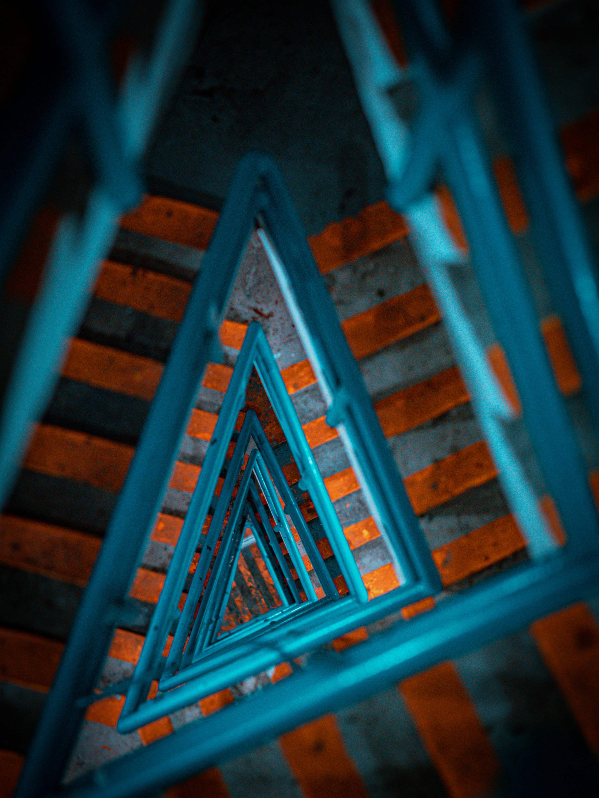 Looking down a spiral staircase with teal railings and orange steps