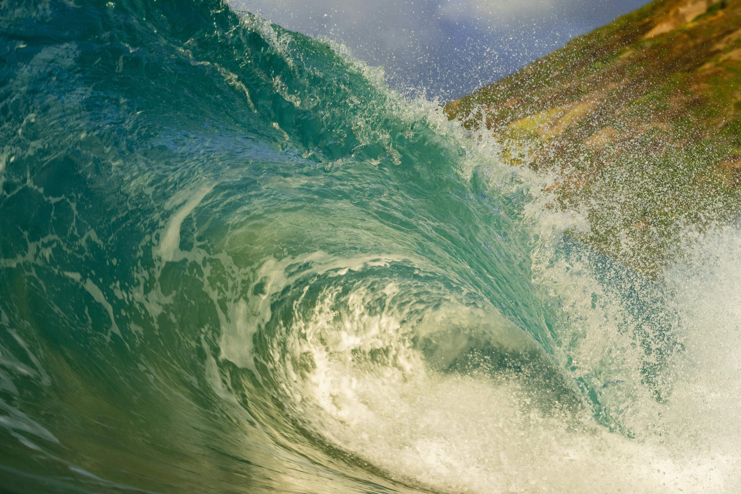 Large green ocean wave crashing near a rocky shoreline