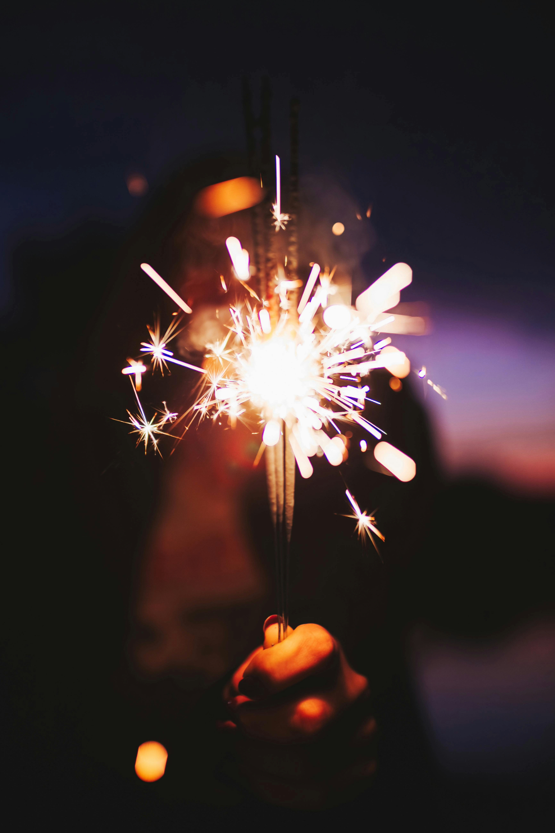 Hand holding a lit sparkler against a dark background